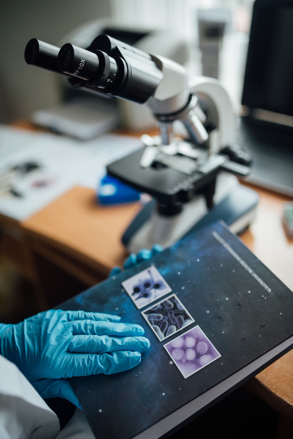 Researcher analyzing microorganisms at a laboratory workstation with a microscope and scientific literature — 동물실험과 작용 방식 3단계